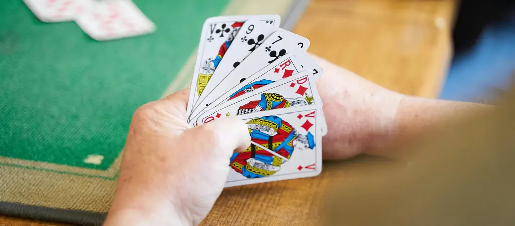 Römi szabályok játék menete, játékos kezében kártyalapok zöld asztalon