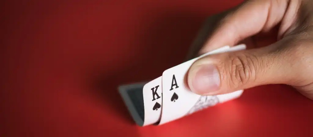 Blackjack szabályok és döntési lehetőségek, játékos kezében ász és király kártya vörös háttéren