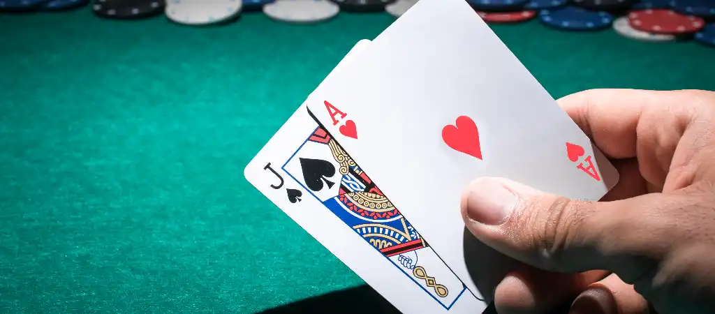 Blackjack szabályok és játékmenet, játékos ász és bubi lapokat tart zöld blackjack asztal felett